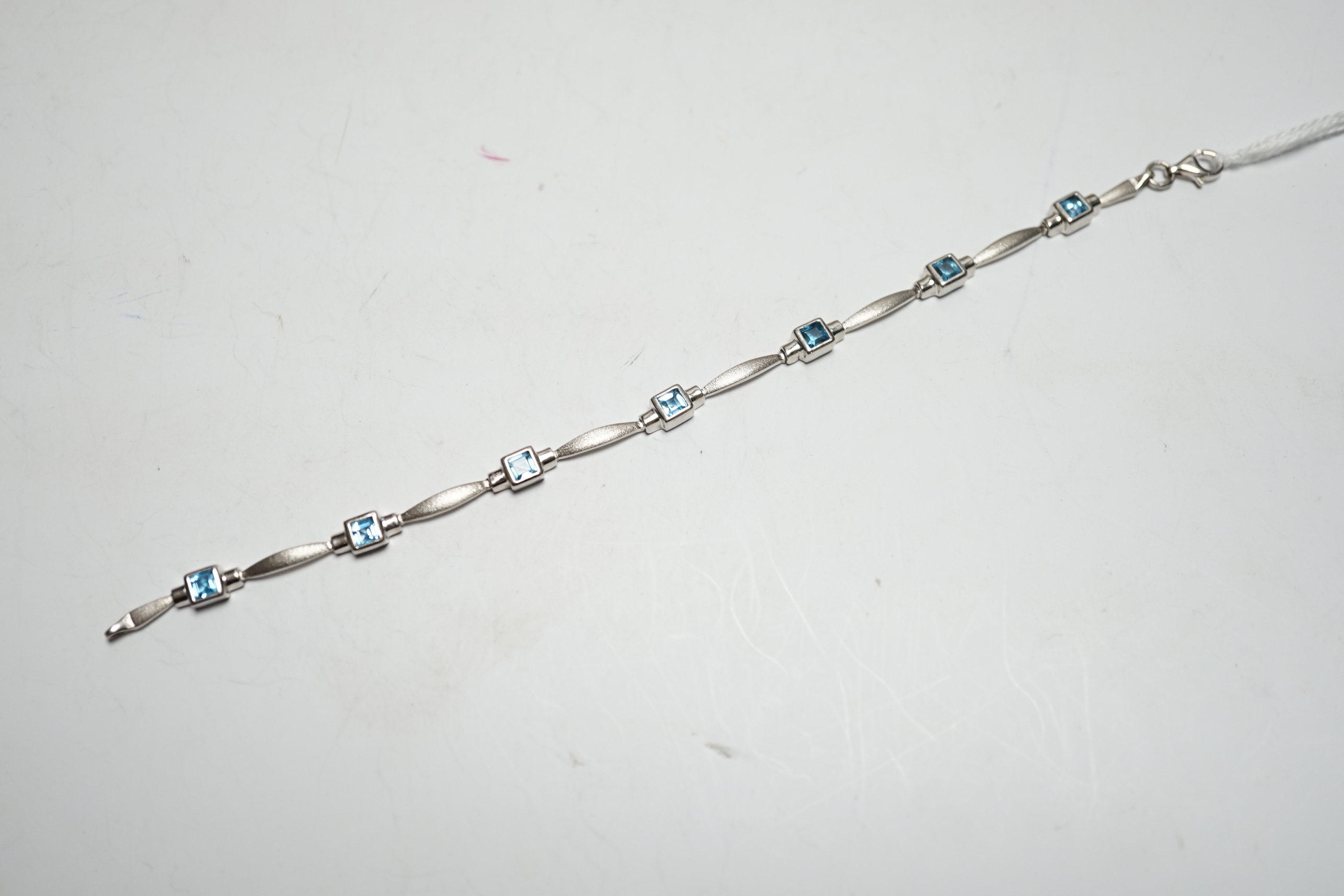 A modern brushed 9ct white gold and seven stone square cut blue topaz? set bracelet, 18cm, gross weight 8.5 grams.